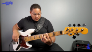 young black man sitting down playing a white bass guitar 
